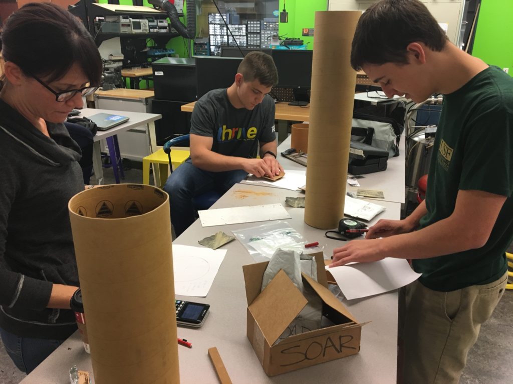 The NSL Prototyping team works in the lab to cut the lander legs out of a piece of rocket tubing and shape them to the desired tapered fit.